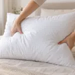 Manos ahuecando una almohada blanca de fibra para recuperar su volumen