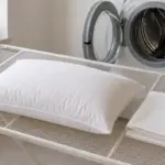 Almohada de fibra extendida en horizontal sobre un tendedero de malla junto a la lavadora