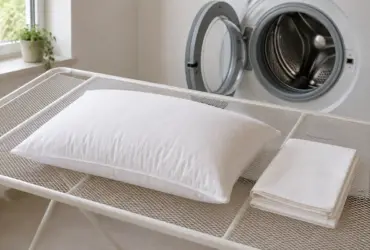 Almohada de fibra extendida en horizontal sobre un tendedero de malla junto a la lavadora